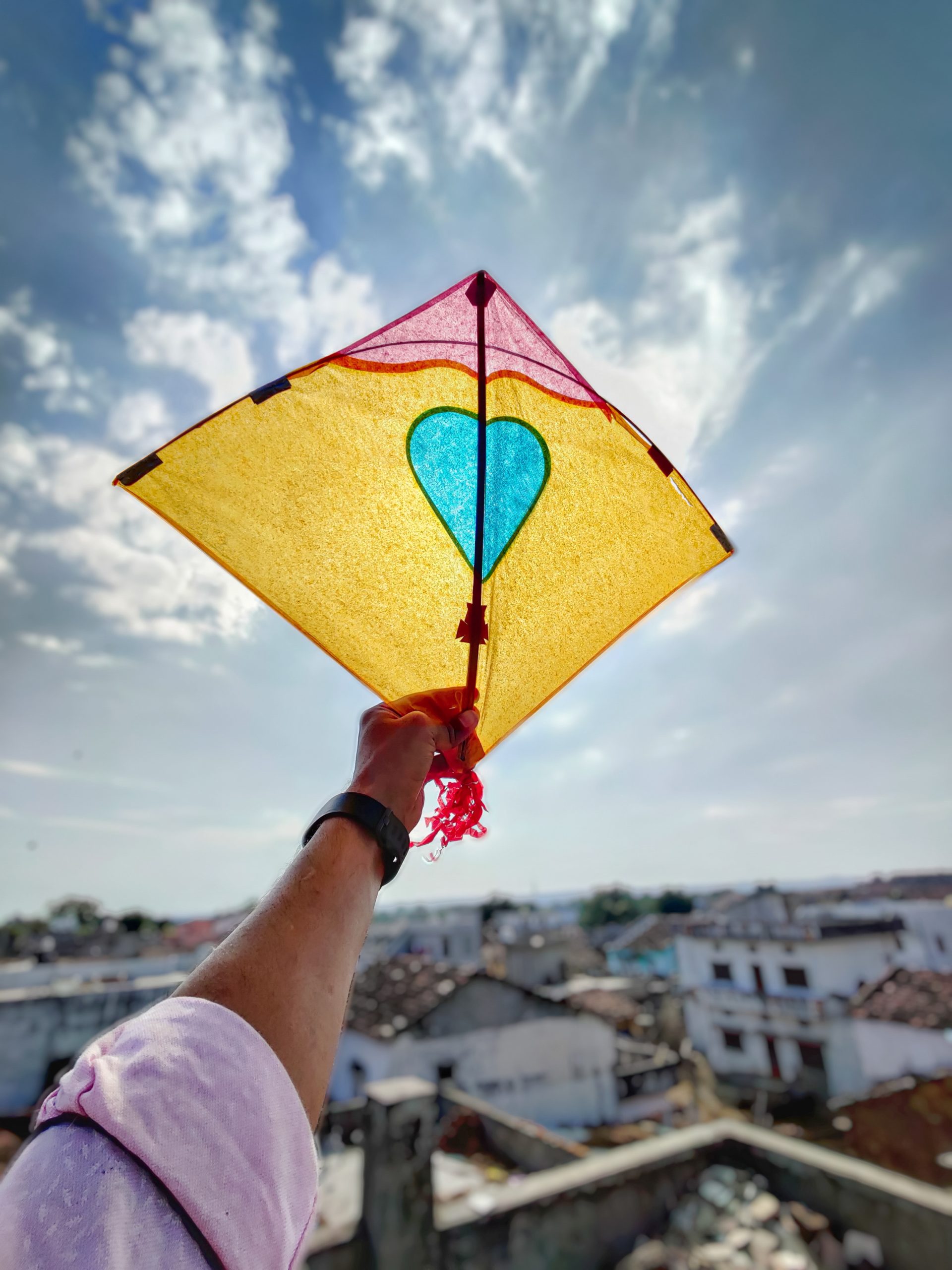 a yellow pink and blue paper kite being held up to a blue sky